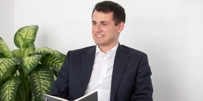Jacob Fay sits at a desk in a meeting room holding a notebook.