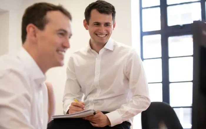 Two team members look at a computer screen smiling.