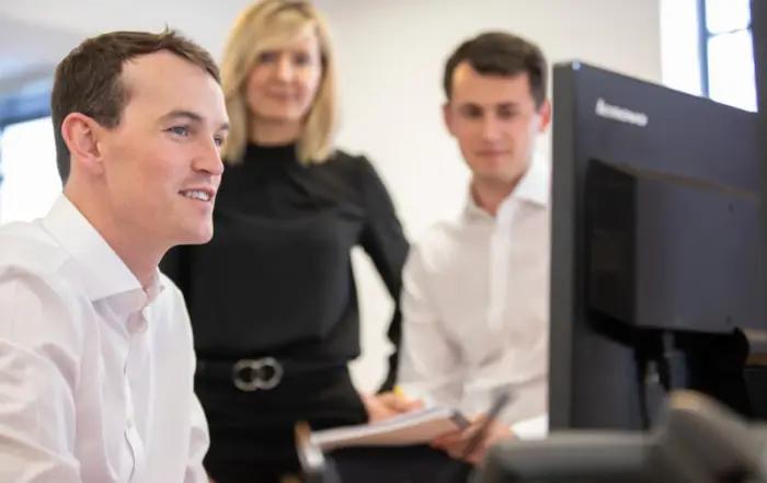 Three members of the John Lamb Hill Oldridge team gather around a monitor to discuss their work.